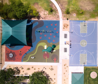 Aerial photo of Michelle Brooks-Totress Park of an artist-designed rubber playground surface, a playground, shade sail, several trees and a basketball court.