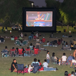 A group of families sits in front of a large screen watching Toy Story at Movies in the Park