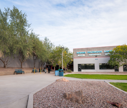 Front entrance of Kiwanis Rec Center with two people walking on the sidewalk on a sunny day.